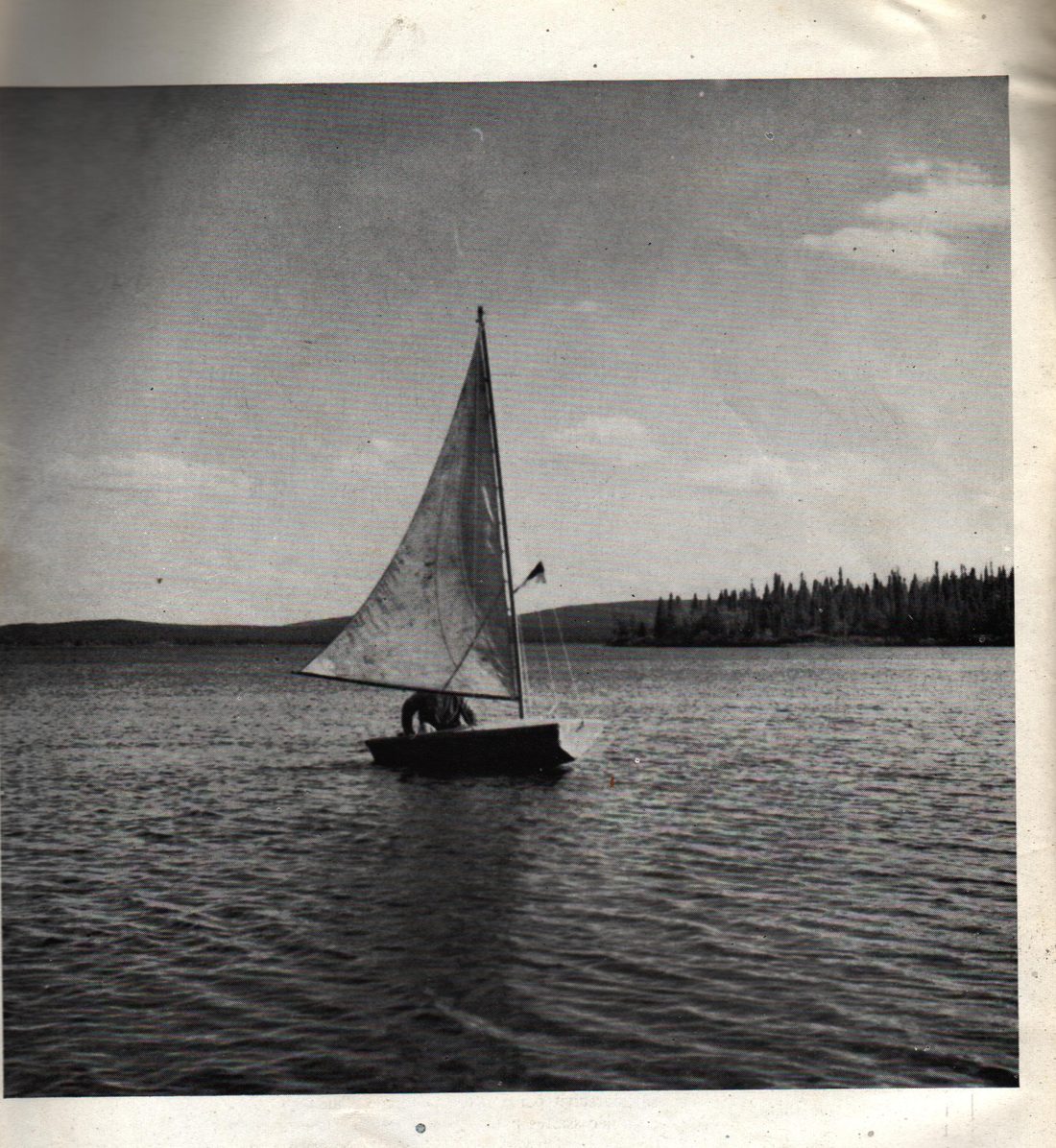 A small sailboat on Carol Lake in 1959, with boreal forest and rolling hills stretching to the horizon under an open sky